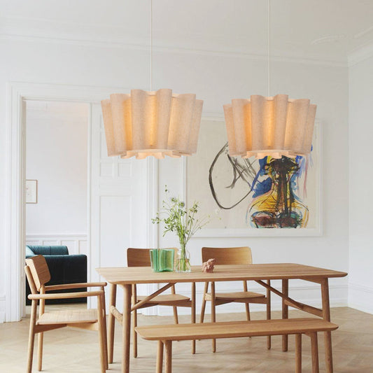 Dining room with wooden table, chairs, and a bench under two large fluted lamps.