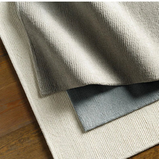 Close-up of textured rug samples in beige, gray, and white on a wooden floor.