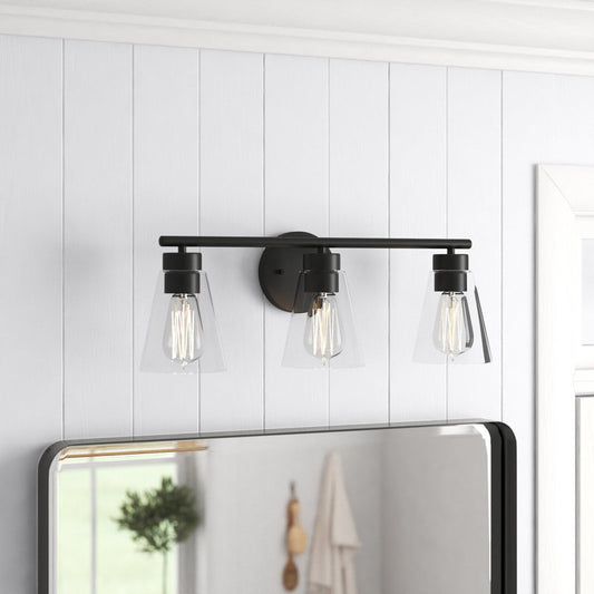Black wall-mounted light fixture with three bulbs on a white paneled wall.